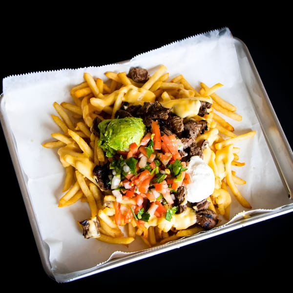 Loaded fries with cheese, steak, guacamole, pico de gallo, and sour cream on a tray.