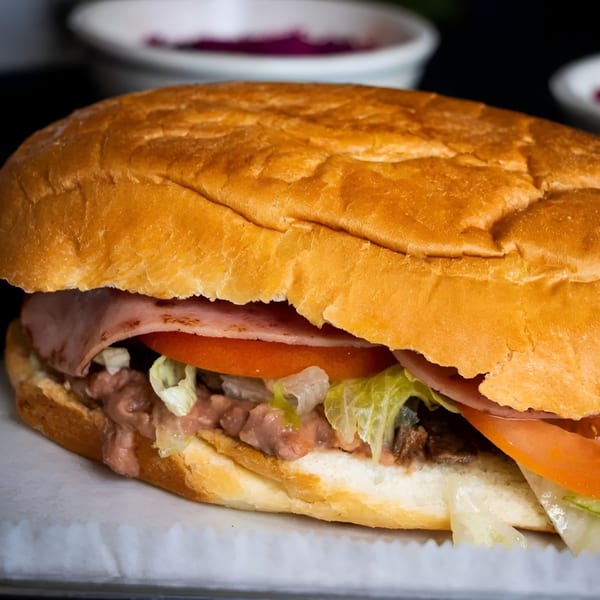 A large torta sandwich filled with ham, lettuce, tomato, and a creamy pink sauce.